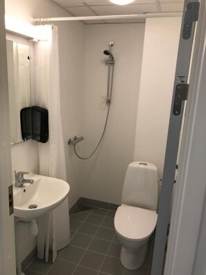 Een kleine, functionele badkamer met een wit wastafel, toilet en douche.