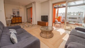 En stue med sofa, sofabord, fjernsyn og en balkon med havemøbler.
