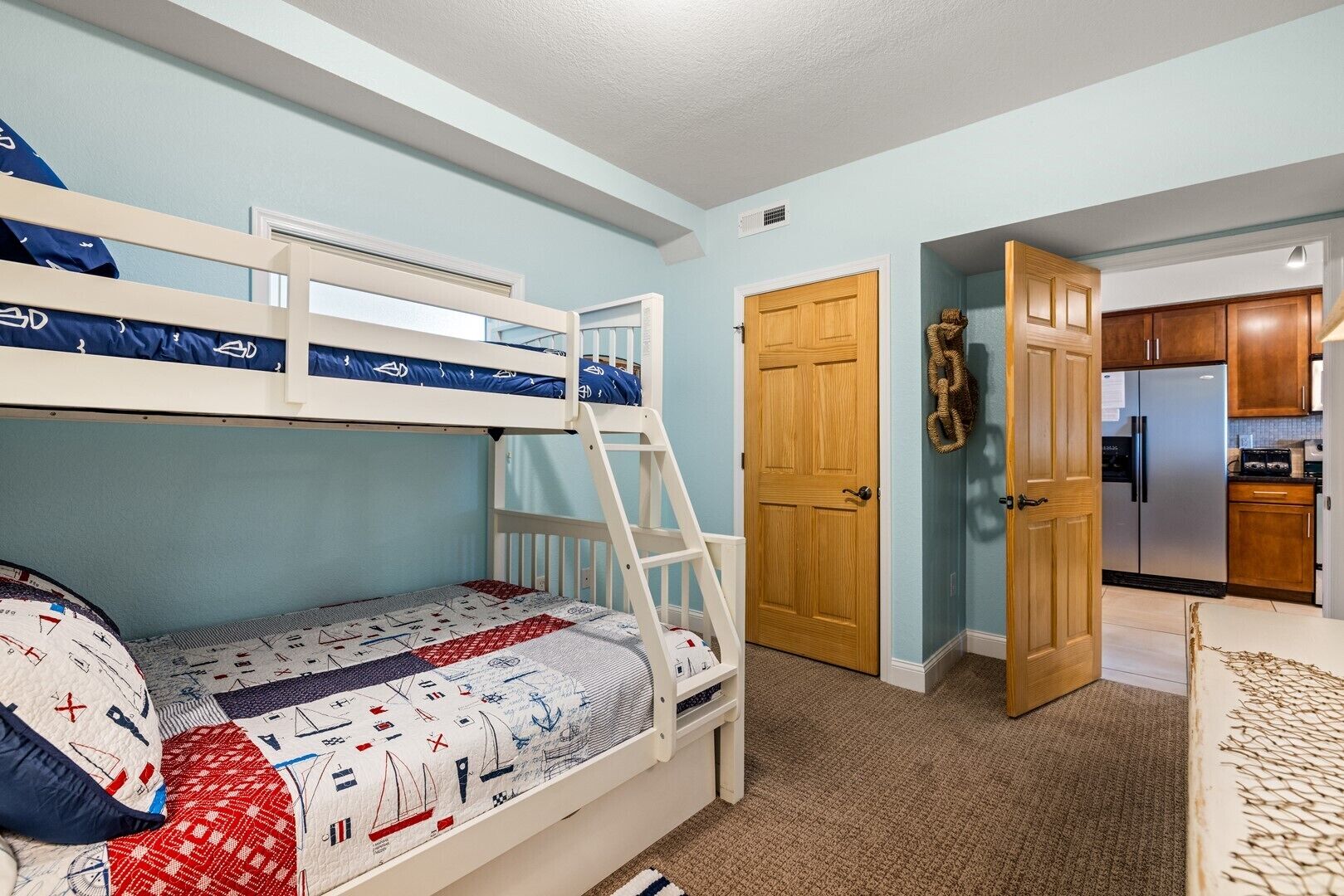 A bedroom with bunk beds, a wooden door, and a kitchen visible through an open door.