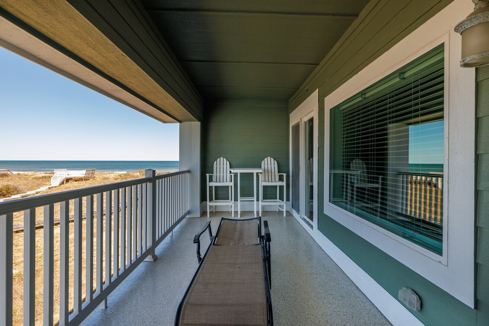 Un balcon avec vue sur la plage, deux fauteuils Adirondack blancs et une petite table.