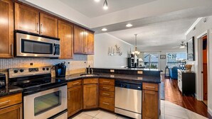 Une cuisine moderne avec des meubles en bois, des appareils électroménagers en acier inoxydable et une vue sur le salon.