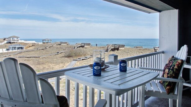 Un balcon avec vue sur la plage, deux chaises, une table et deux bouteilles de bière.