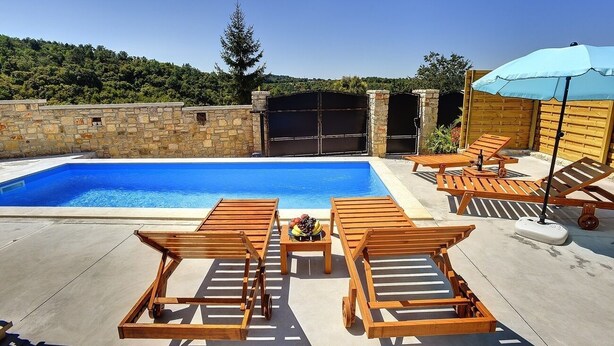 Ein Swimmingpool mit Holzliegen und einem Tisch, umgeben von Steinmauern und einem Holzzaun.