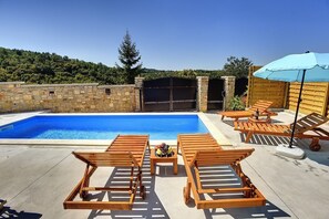 Una piscina con sillones de madera y una mesa, rodeada de muros de piedra y una valla de madera.