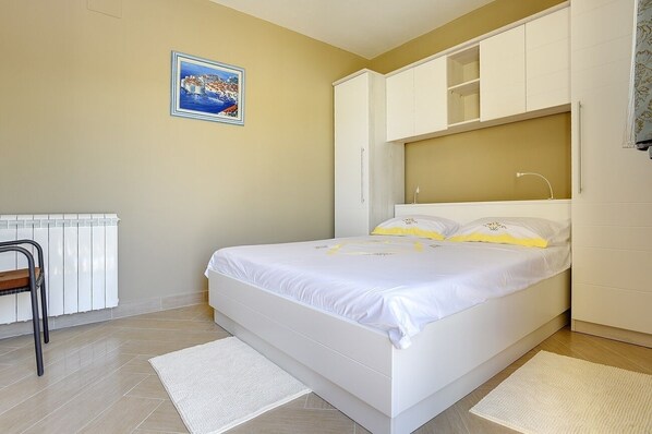 Un dormitorio con cama, armarios blancos, un radiador y un cuadro en la pared.