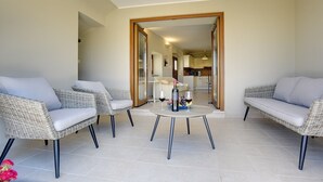 Ein Zimmer mit zwei Korbschaukeln, einem runden Tisch mit Flasche und Gläsern sowie Blickrichtung in eine Küche und einen Essbereich.