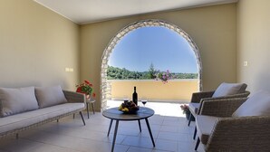 Ein Balkon mit einer Rattan-Sofa, einem runden Tisch mit einer Flasche und Gläsern sowie Blick ins Grüne.