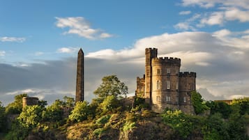 Un château historique doté d’une haute tour et d’un obélisque imposant, le tout entouré d’une végétation luxuriante.
