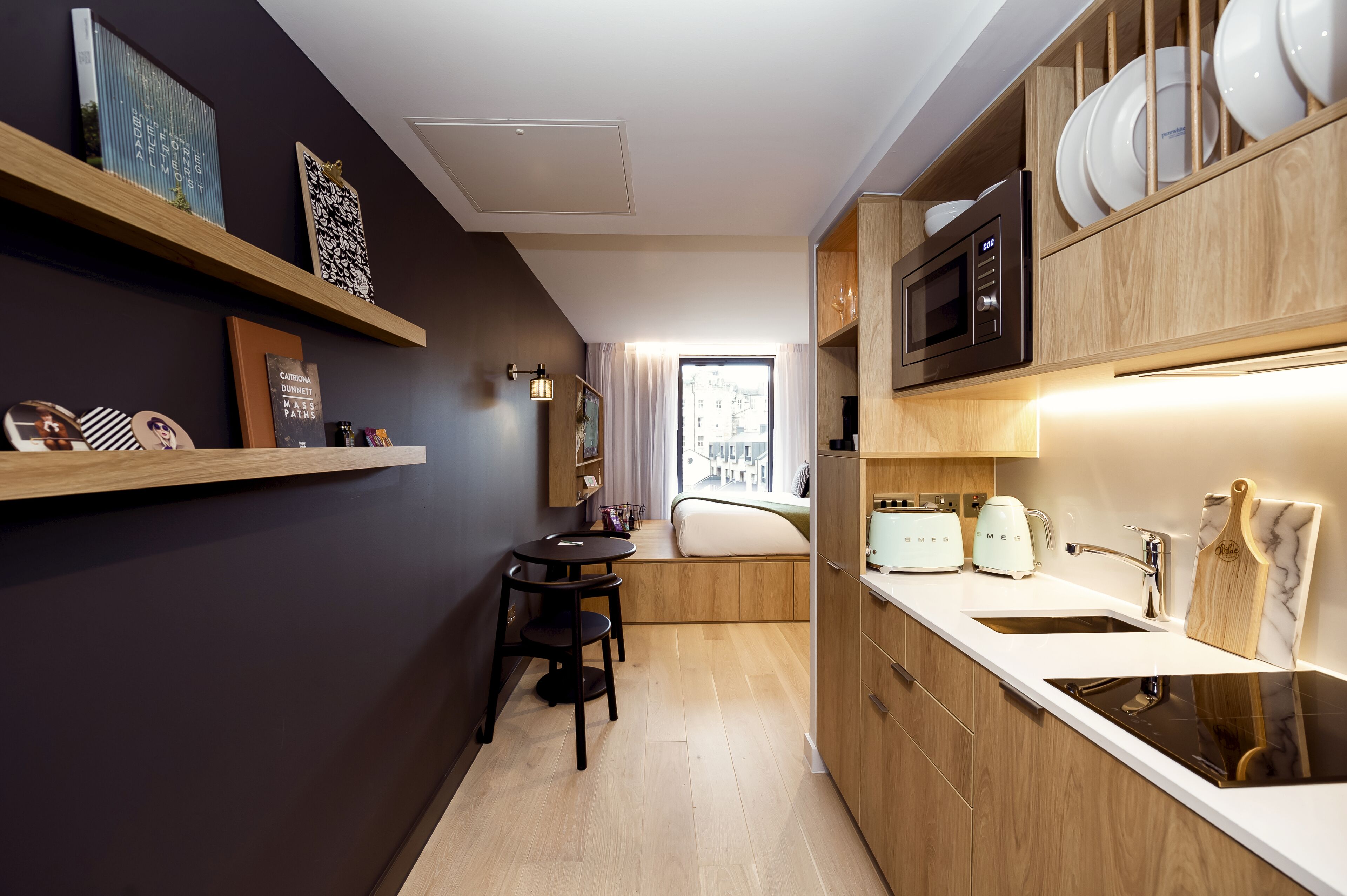 Una cucina funzionale con mobili in legno, un forno a microonde integrato e un lavello. È presente una piccola zona pranzo con tavolo e sedie.