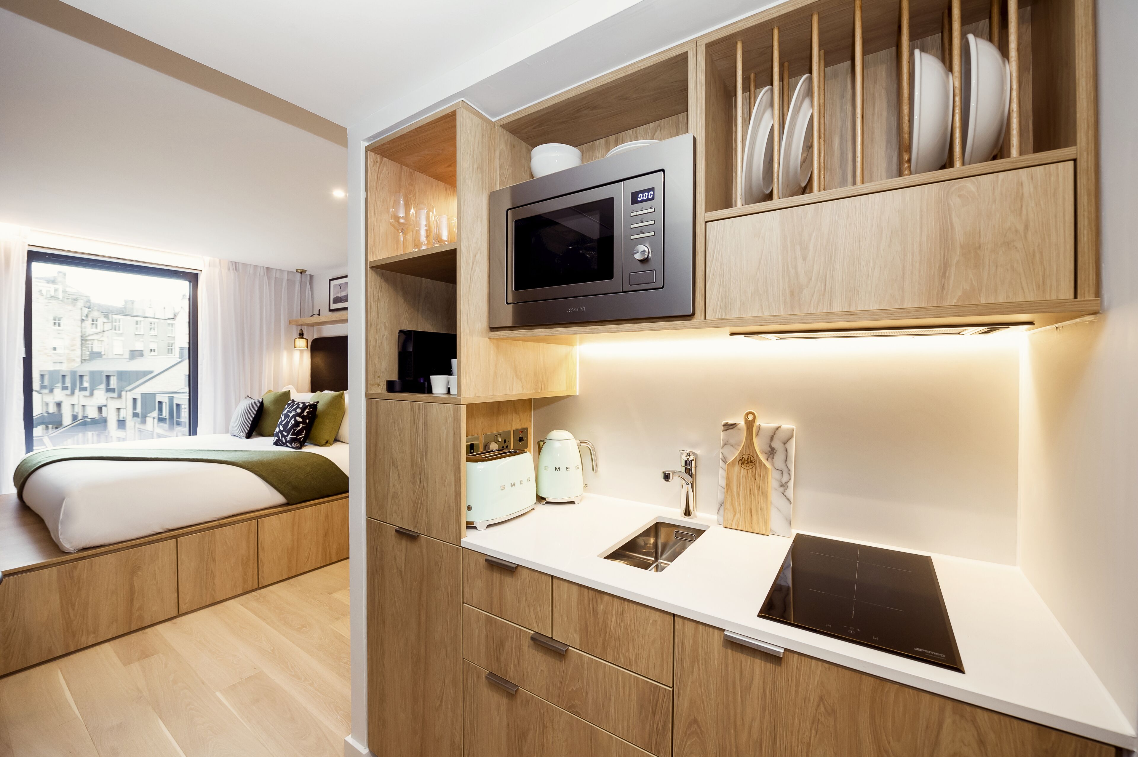 A compact bedroom with a bed, a built-in wardrobe, and a small kitchenette with a microwave, toaster, and sink.
