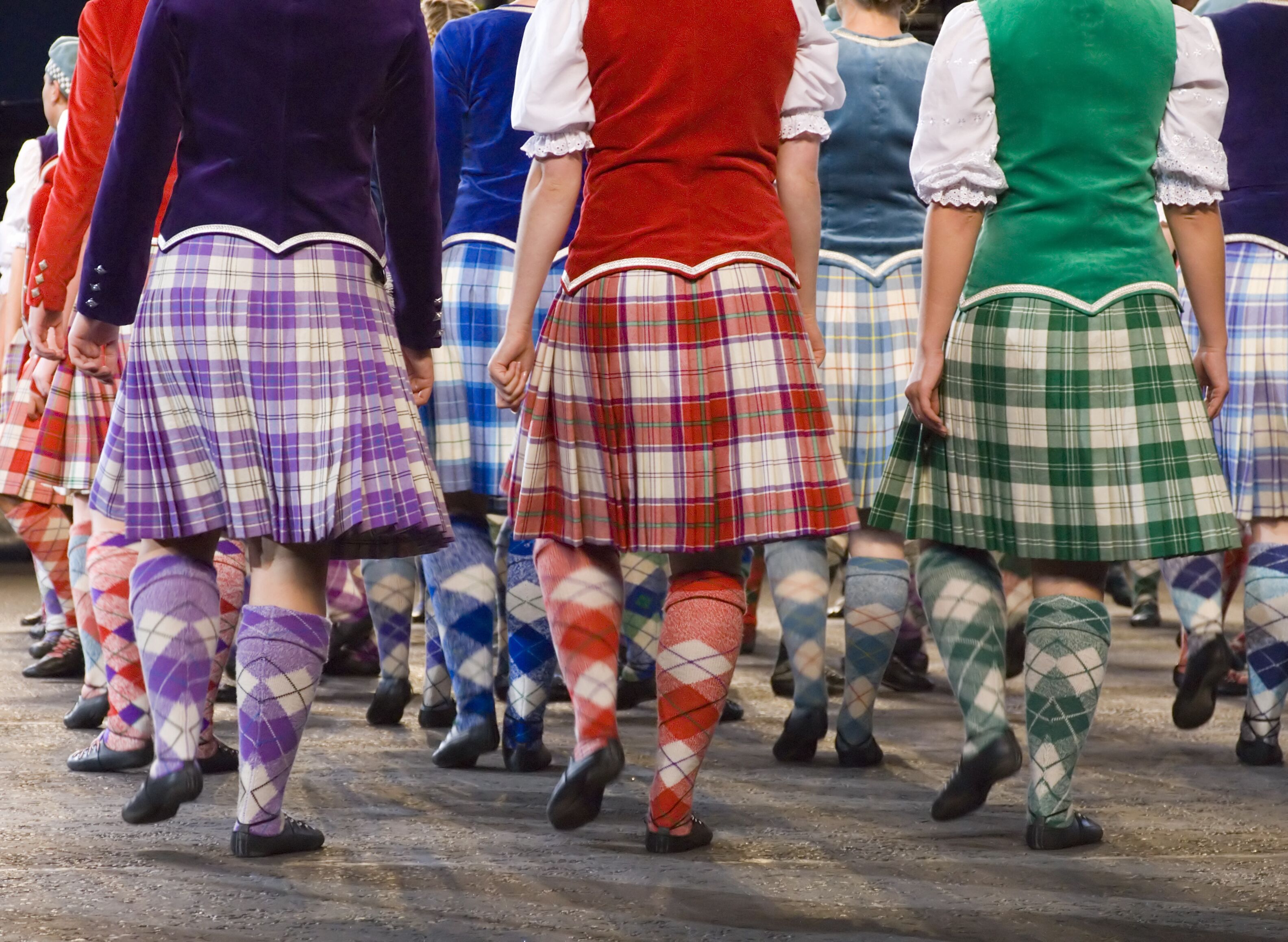 A group of people in traditional Scottish attire, including kilts and knee-high socks, walking in a line.