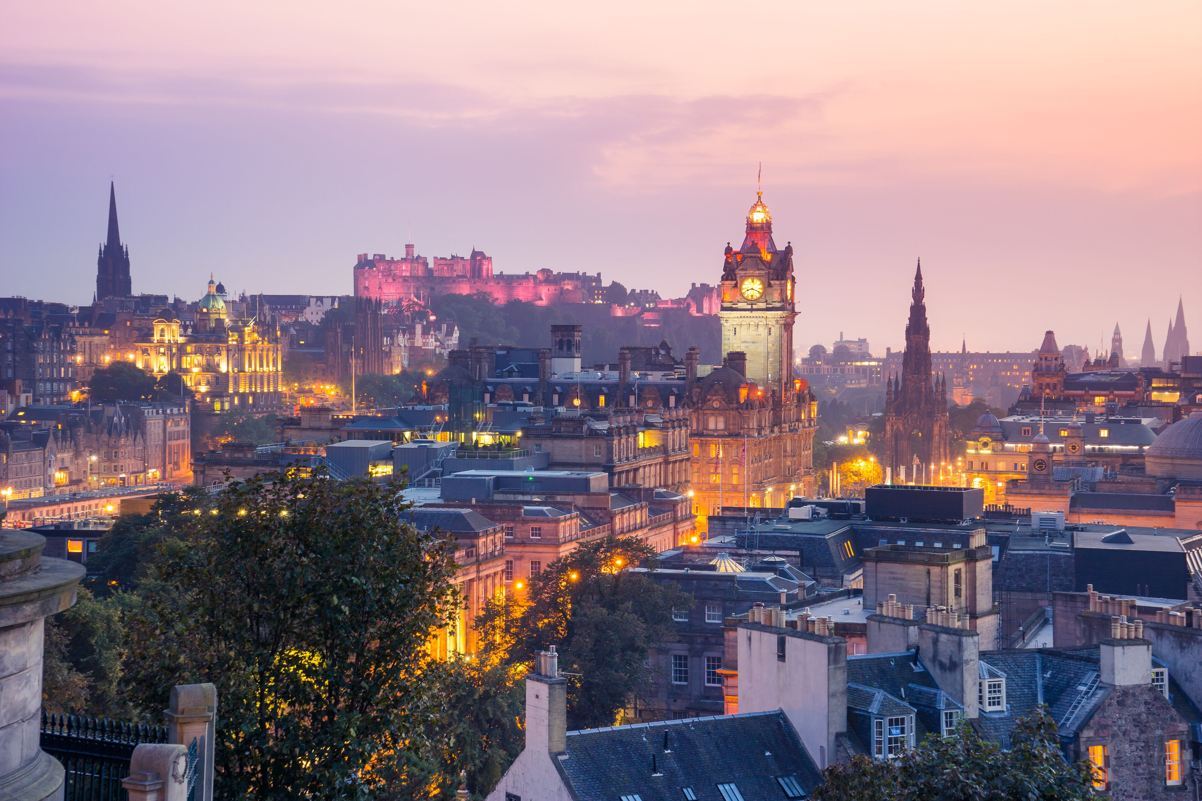 A cityscape at dusk with illuminated buildings and a prominent clock tower.