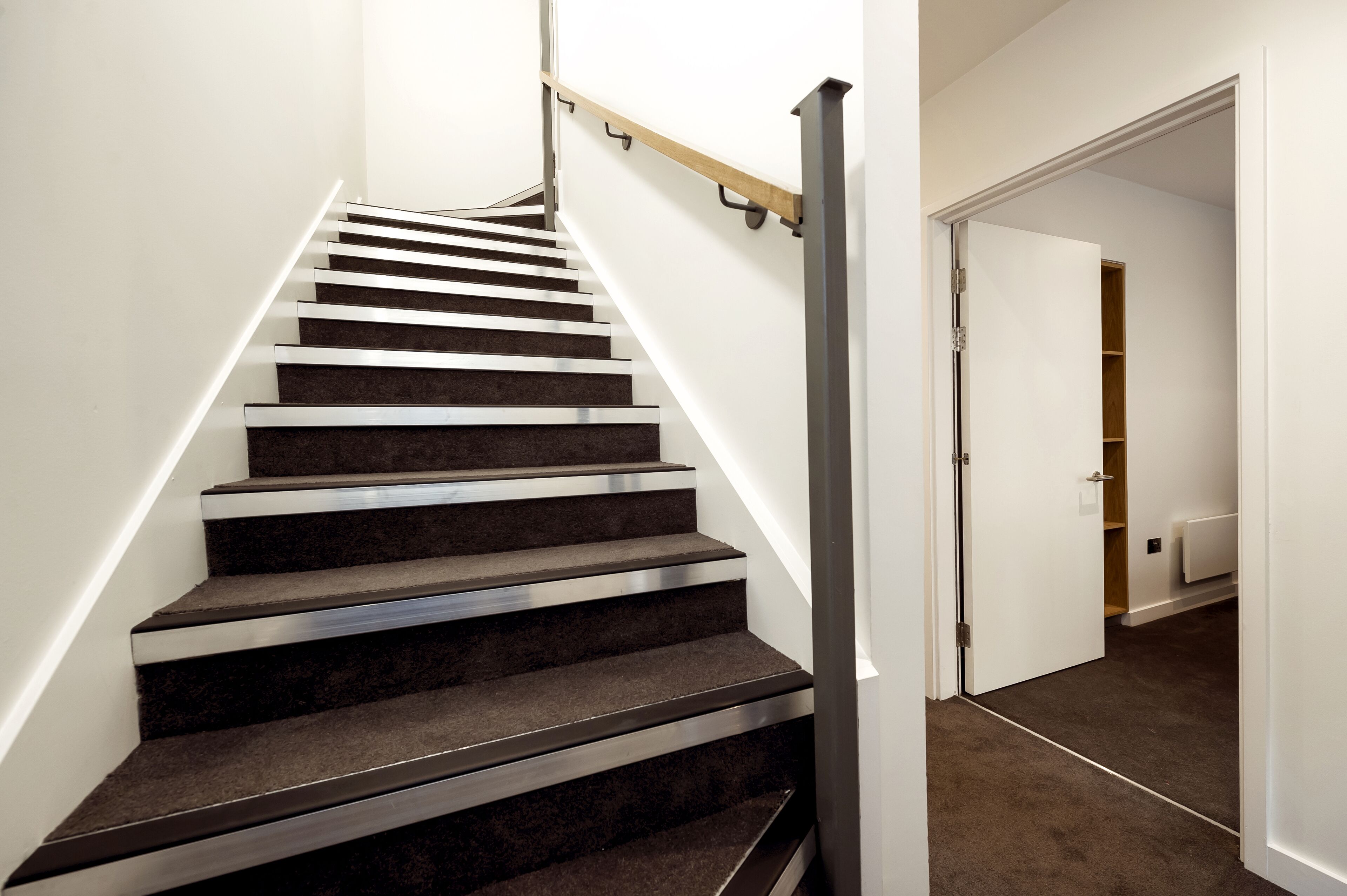 A staircase with a handrail, carpeted steps, and a white wall.