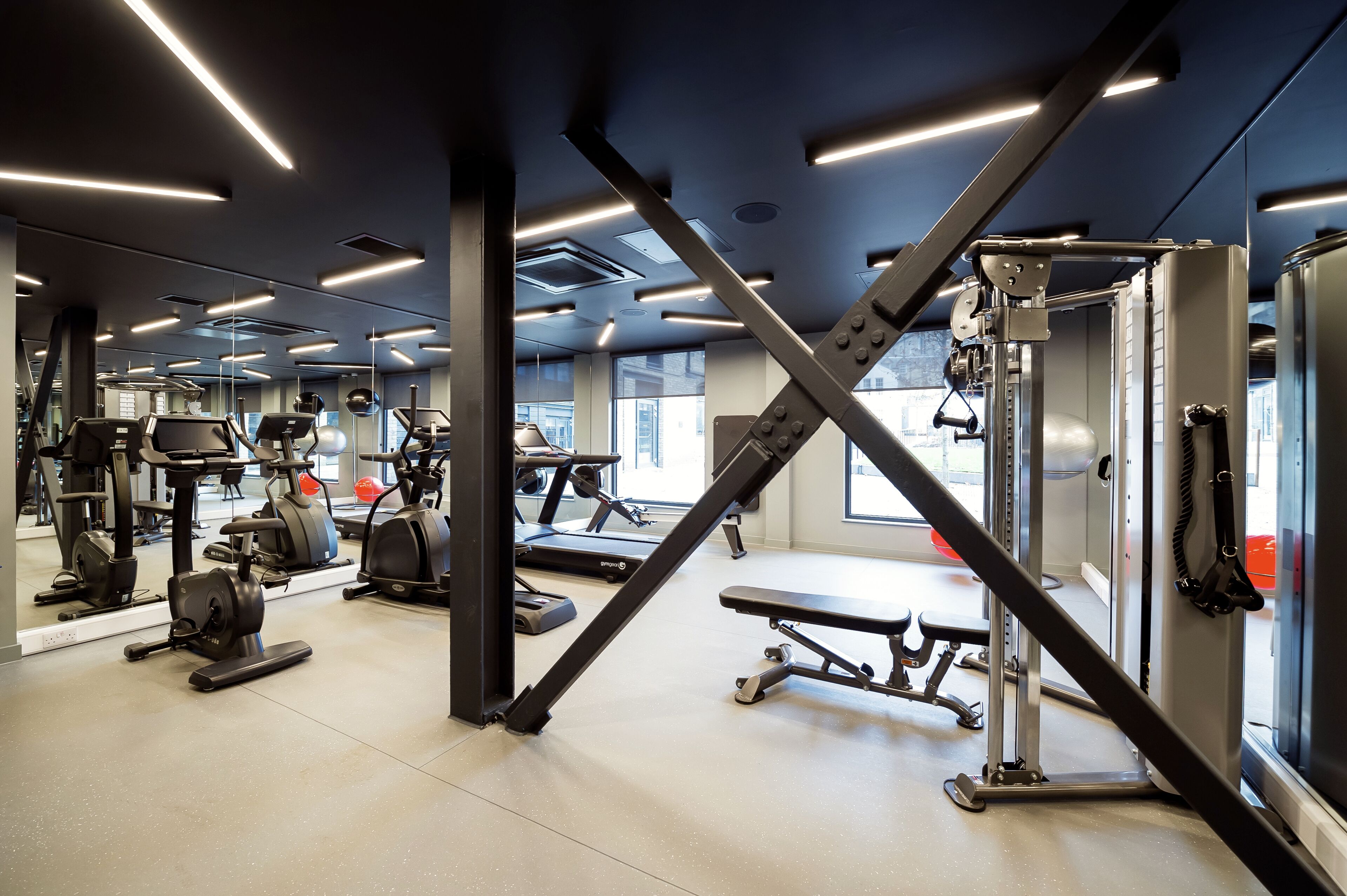 A modern gym with various exercise equipment, large windows, and a clean, well-lit interior.