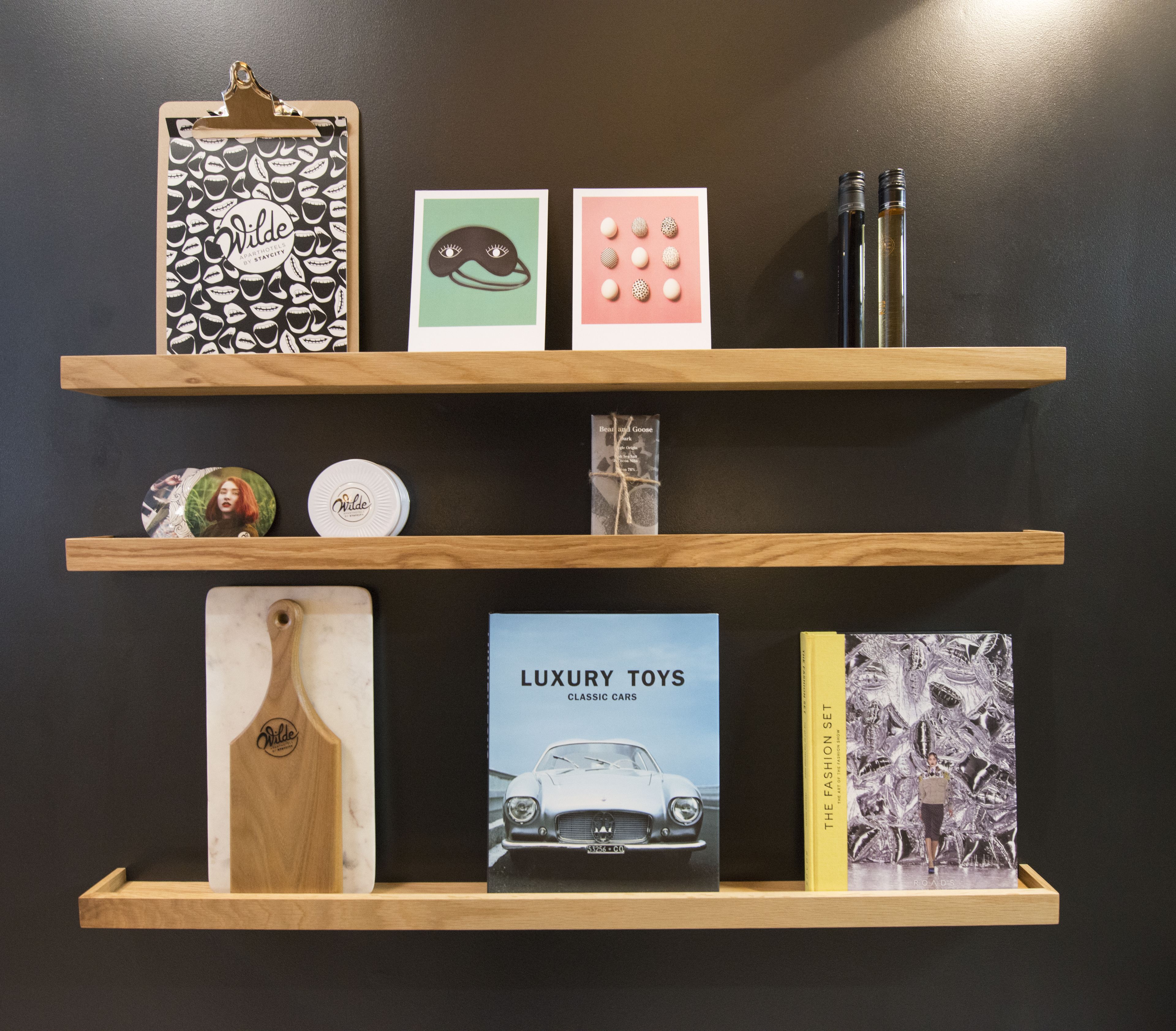 Three wooden shelves with various items including books, a bottle, and decorative objects.