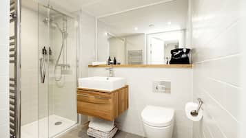 Un baño moderno con ducha de vidrio, lavabo blanco con gabinete de madera y retrete.
