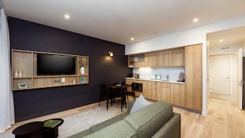 Ein modernes Wohnzimmer mit Flachbildfernseher, einem grünen Sofa, einem kleinen Couchtisch und einem Essbereich mit Tisch und Stühlen.