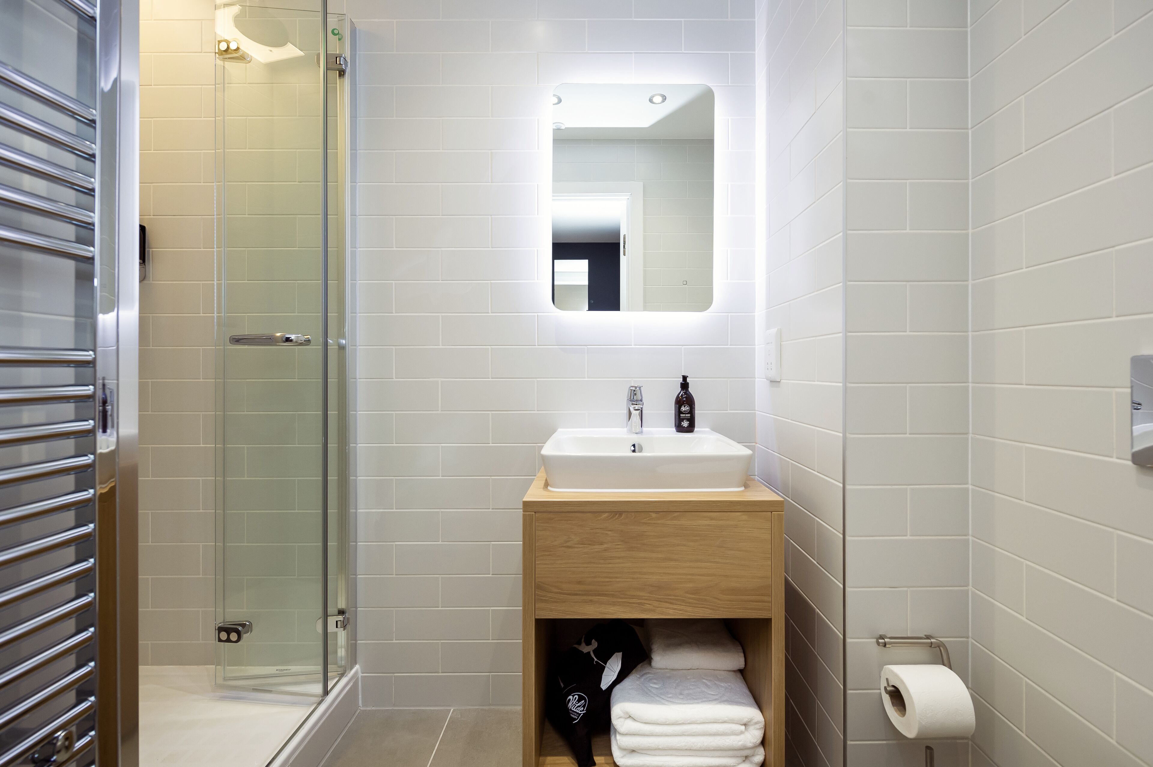 Een moderne badkamer met een glazen douche, een wastafel met spiegel en een handdoekrek.