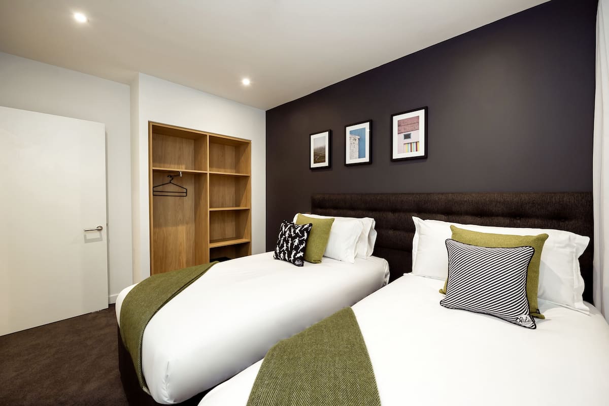 A hotel room with two beds, a wardrobe, and three framed pictures on the wall.