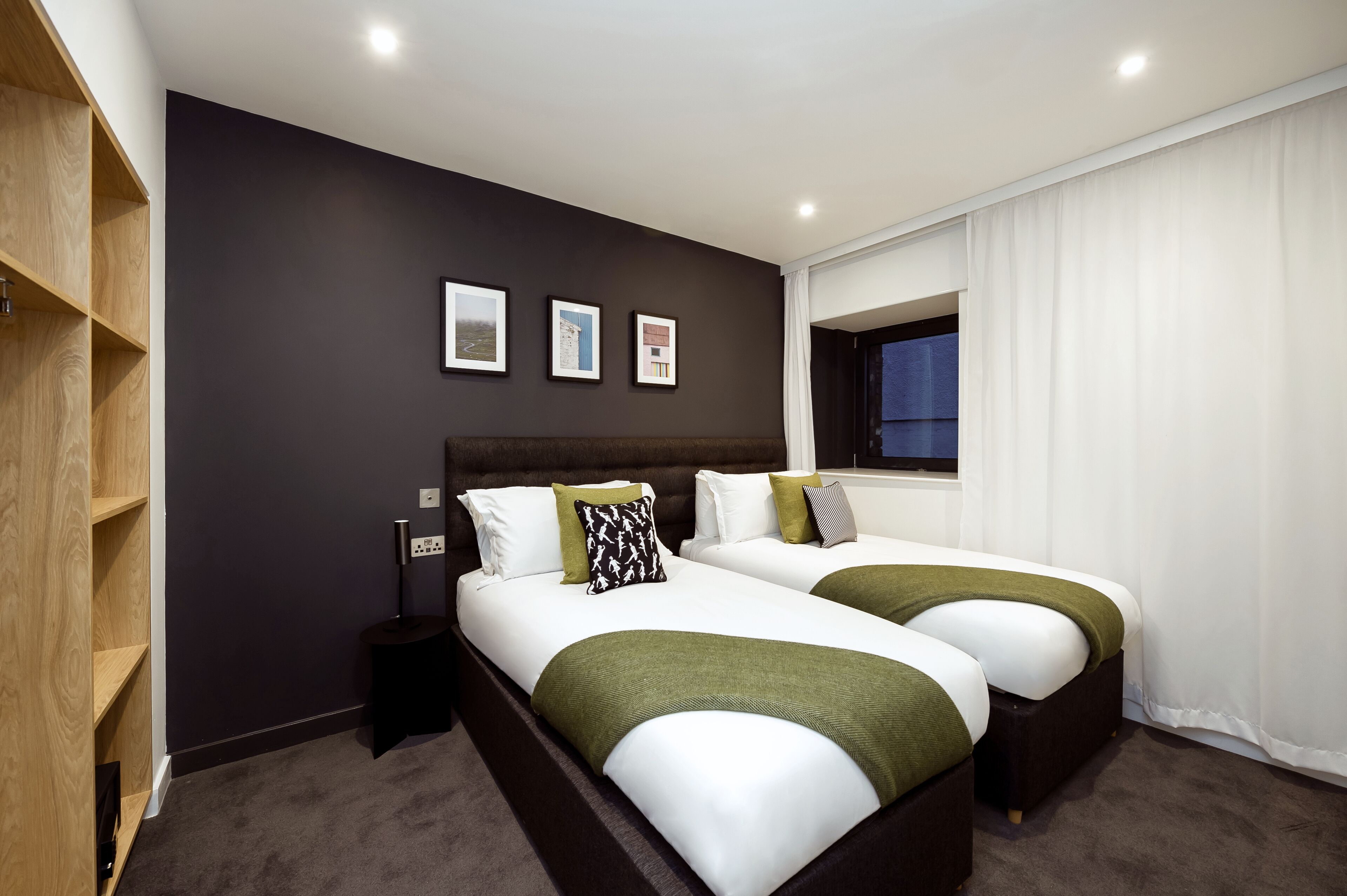 A hotel room with two beds, a dark wall, and a window with white curtains.