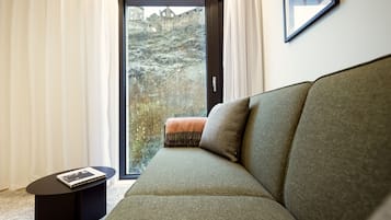A modern living room with a green sofa, a small black side table, and a view of a rocky hillside through a glass door.