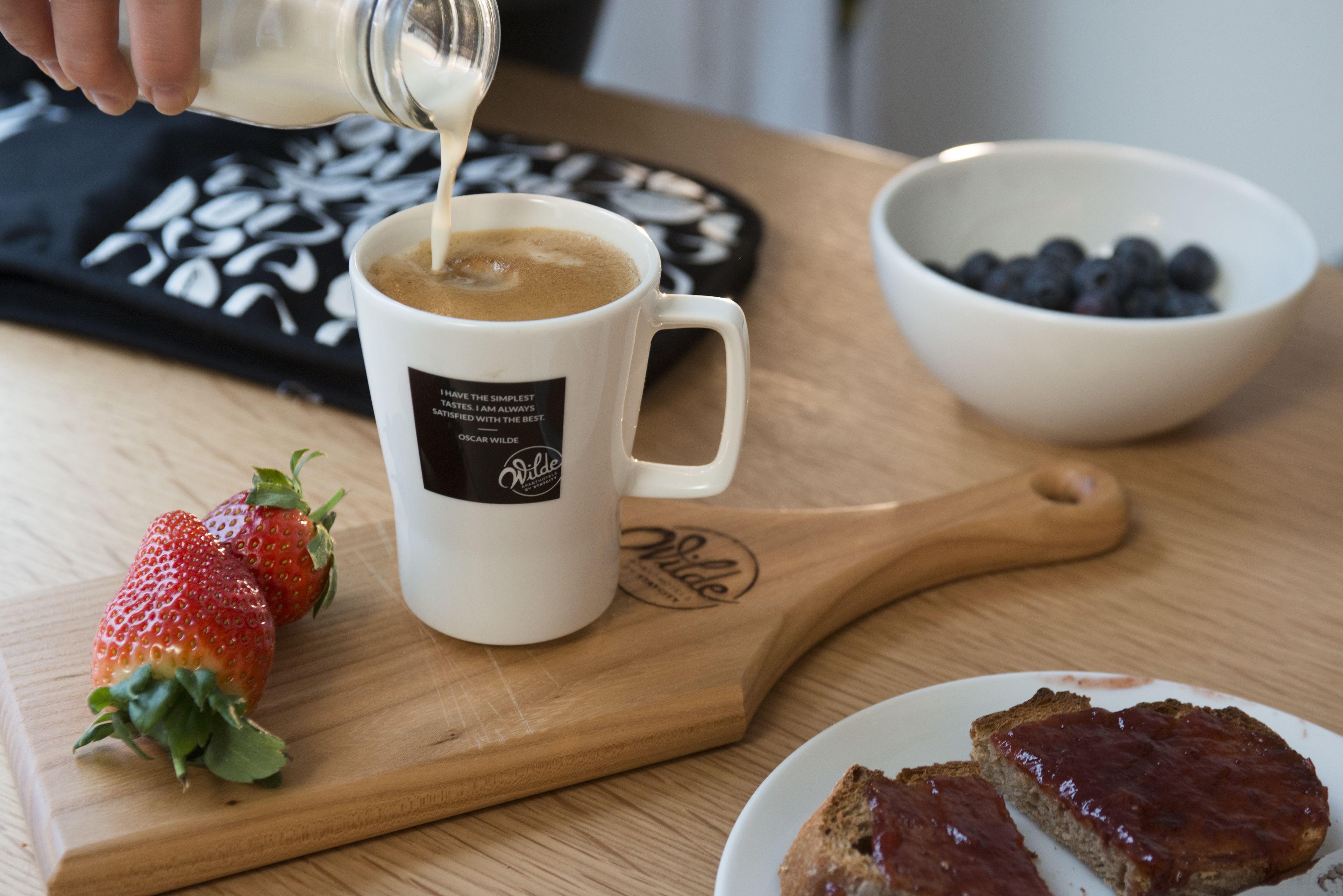 A coffee mug on a wooden board, a bowl of blueberries, and a plate with toast.