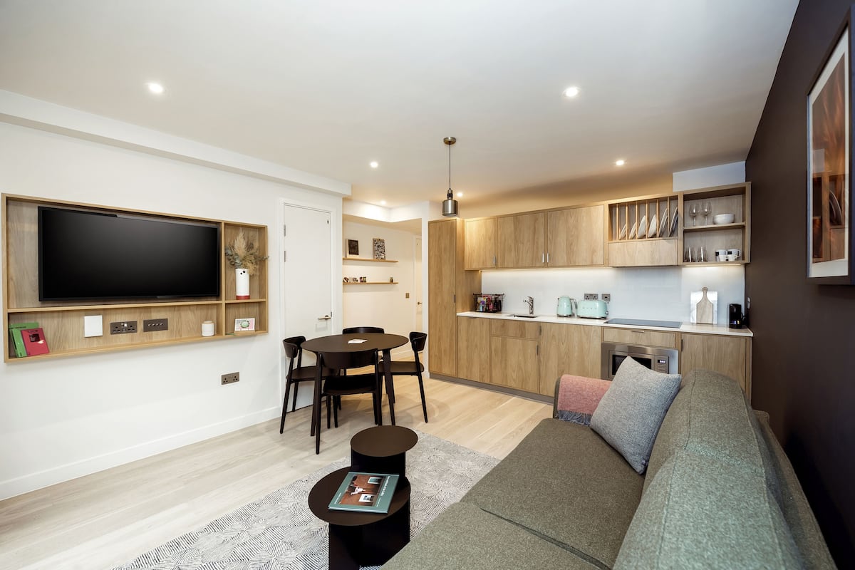 A modern living room with a flat-screen TV, a dining area, and a kitchenette.
