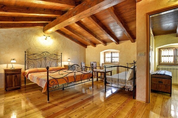 A bedroom with a wooden ceiling, a bed with a metal frame, a nightstand, a chair, and a window with curtains.