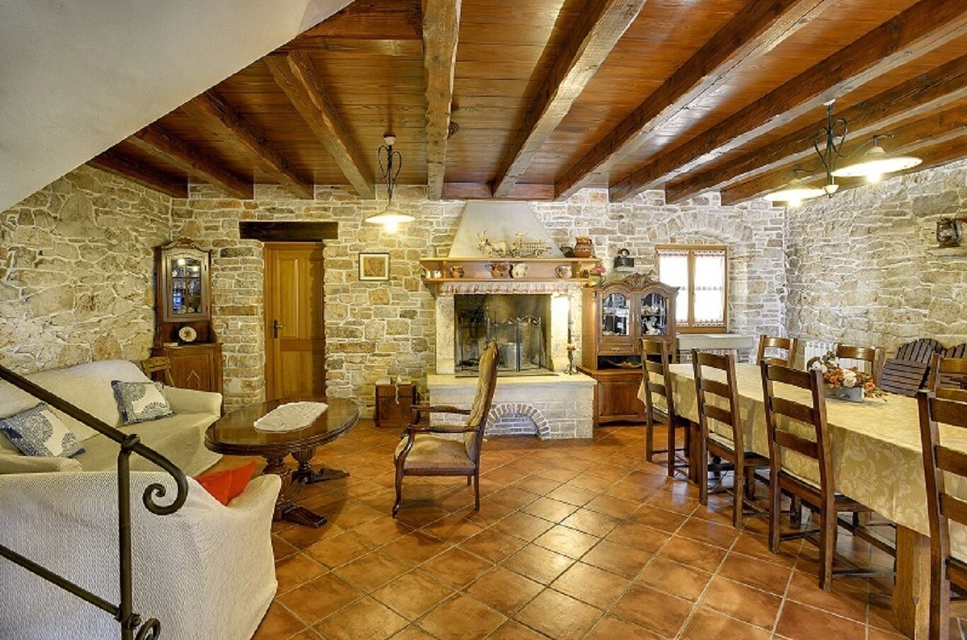 A rustic stone interior with a fireplace, wooden beams, a dining area, and a sofa.