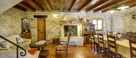 A rustic stone interior with a fireplace, wooden beams, a dining area, and a sofa.