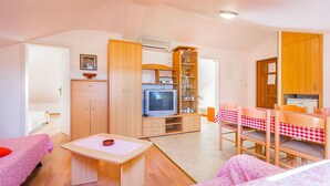 Un ambiente compatto con angolo cottura, zona pranzo con tovaglia a scacchi, televisione e letto con copripiumino a fiori rosa.