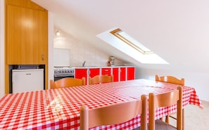 A compact kitchen with a red and white checkered tablecloth, a small refrigerator, and a skylight above the dining area.