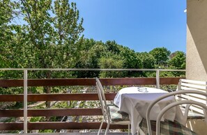Un balcón con mesa y sillas, con vistas a un jardín con árboles y cielo despejado.