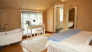 A bedroom with a large bed, a white vanity with a mirror, a bathtub, and a chandelier. - Luxury 5-star single-storey cottage for two near the Cornish coast (Helston)