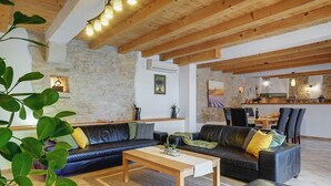 Un salon moderne avec un mur en pierre, des poutres en bois au plafond, un ensemble de canapés et un coin repas comprenant des chaises et une table.