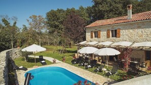 Un bâtiment en pierre doté d’une piscine, d’un espace extérieur aménagé et de parasols.