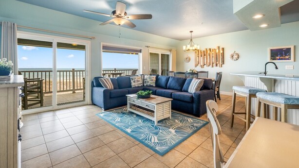 A spacious living room with a large sofa, a coffee table, and a view of the ocean through large sliding doors. - FFR205 - Beach Therapy by First Flight Rentals (Kill Devil Hills, NC 27948)