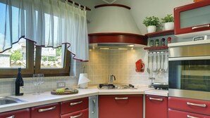 A kitchen with red cabinets, a stainless steel oven, and a window with white curtains. - Sunny villa 500 meters to beach with private pool (Peroj)