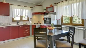 A modern kitchen with red cabinets, a dining table, and a TV. - Sunny villa 500 meters to beach with private pool (Peroj)