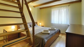 A bedroom with a wooden staircase, a bed with a patterned bedspread, a bedside table with a lamp, and a window with curtains. - Sunny villa 500 meters to beach with private pool (Peroj)