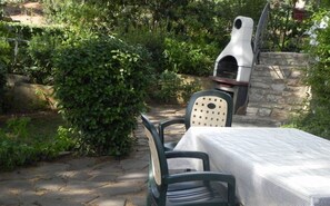 Une terrasse extérieure avec une table et des chaises en pierre, un mur en pierre et un four à pizza.