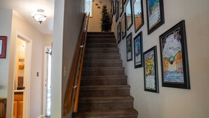 A carpeted staircase with a wooden handrail, leading to a landing with a wall of framed artwork.