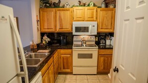 A kitchen with wooden cabinets, a white microwave, a stove, and a sink.