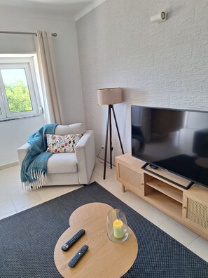 Una sala de estar moderna con un sofá, un televisor, una lámpara y una vela sobre una mesa.