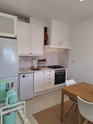 A compact kitchen with white cabinetry, a built-in gas stove, a dishwasher, and a coffee maker.