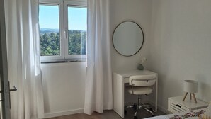 A bedroom with a bed, a desk, a mirror, and a window with curtains.