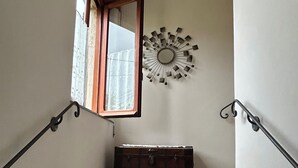 A staircase with a wooden bench at the bottom, a wall-mounted mirror, and a window with a curtain. - LUMIERE LIFE, cozy and bright living room in Castelnuovo Magra  (Castelnuovo Magra)
