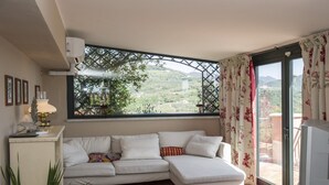 A living room with a white sofa, a TV, and a window with a view of a green landscape. - LUMIERE LIFE, cozy and bright living room in Castelnuovo Magra  (Castelnuovo Magra)