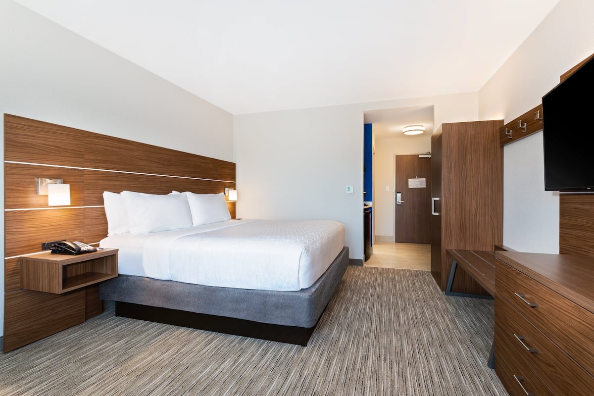 A modern hotel room with a large bed, bedside tables, a flat-screen TV, and a wardrobe.
