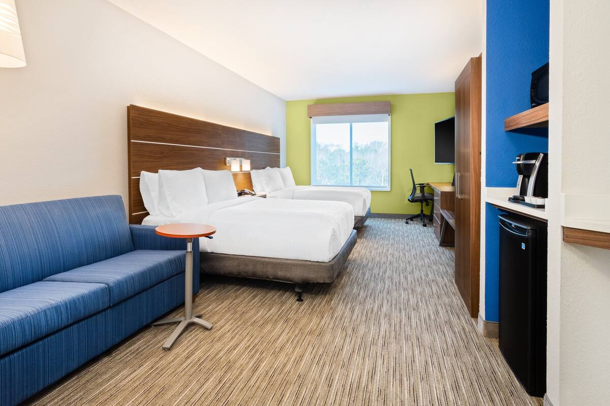A hotel room with two beds, a sofa, a small table, a desk, a TV, and a refrigerator.